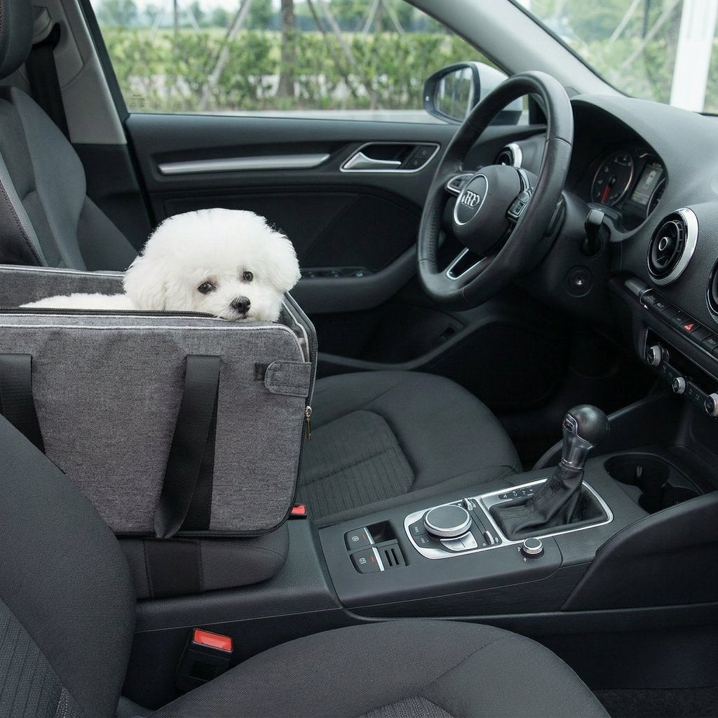 Small white fluffy dog rests in a gray center console dog car seat and portable carrier inside a black car interior.