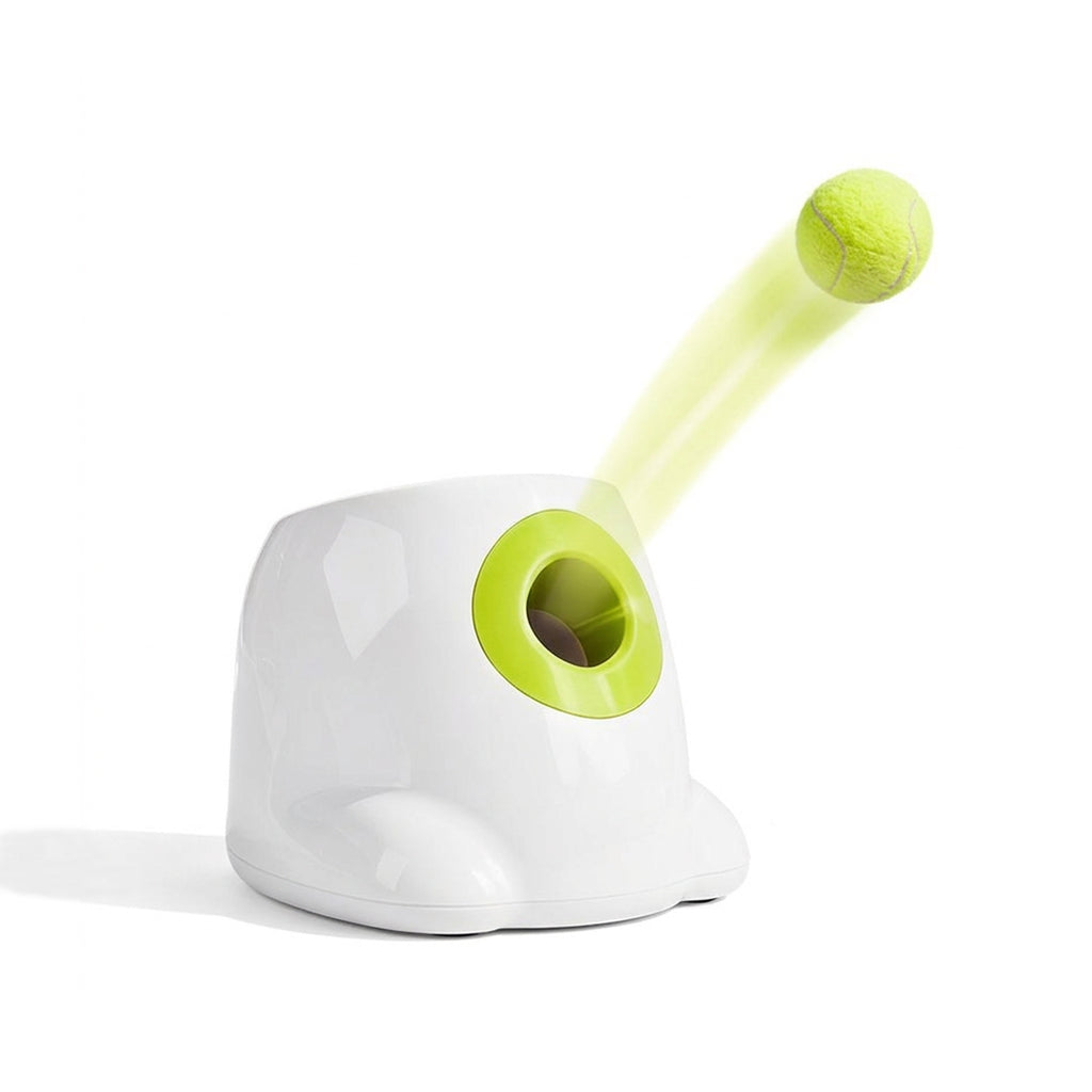 White automatic dog ball launcher with a lime green opening launching a yellow tennis ball on a white background.