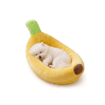 Small white fluffy puppy sleeping peacefully inside a soft yellow banana-shaped dog bed on a white background.