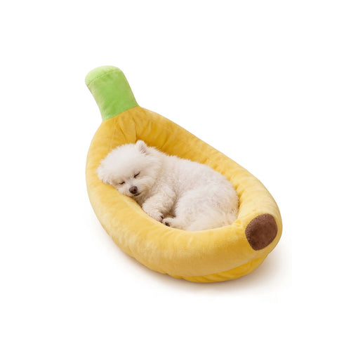 Small white fluffy puppy sleeping peacefully inside a soft yellow banana-shaped dog bed on a white background.