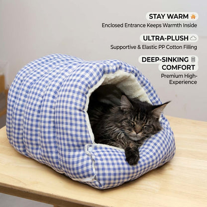 Tabby cat resting inside a blue gingham cave pet bed on a wooden table.