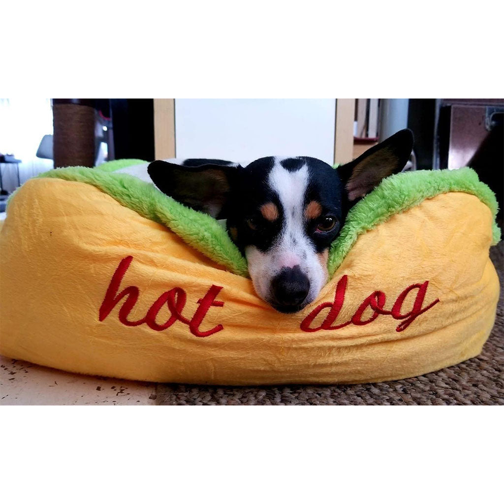 Small black and white dog resting behind the raised yellow rim of the hot dog pet bed.