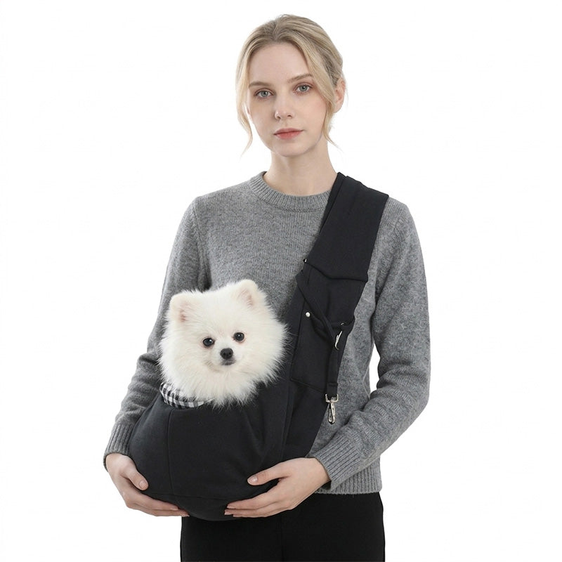 Woman wearing a black pet sling carrier holding a white Pomeranian with wide crossbody strap.