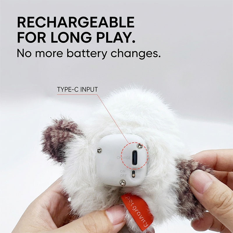 A close-up of a hand opening the bottom of the snowy owl toy to reveal the white electronic mechanism with a Type-C input for recharging, and a red PawsMore brand tag visible.