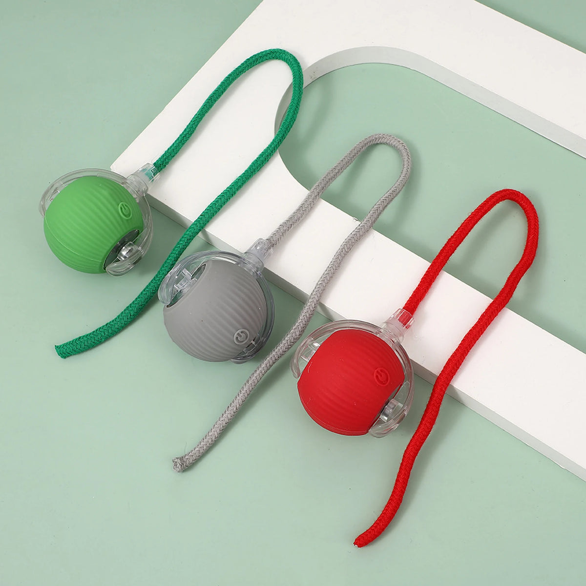 Green, gray and red cat balls with matching rope tails on a pale green background.