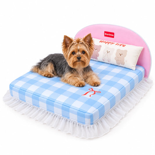 Yorkshire Terrier lying on a blue gingham dog bed with pink headboard, bear pillow and white ruffled skirt