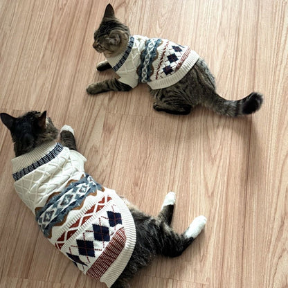 Two tabby cats indoors wearing oat beige Fair Isle knit pet sweaters with ribbed necklines.