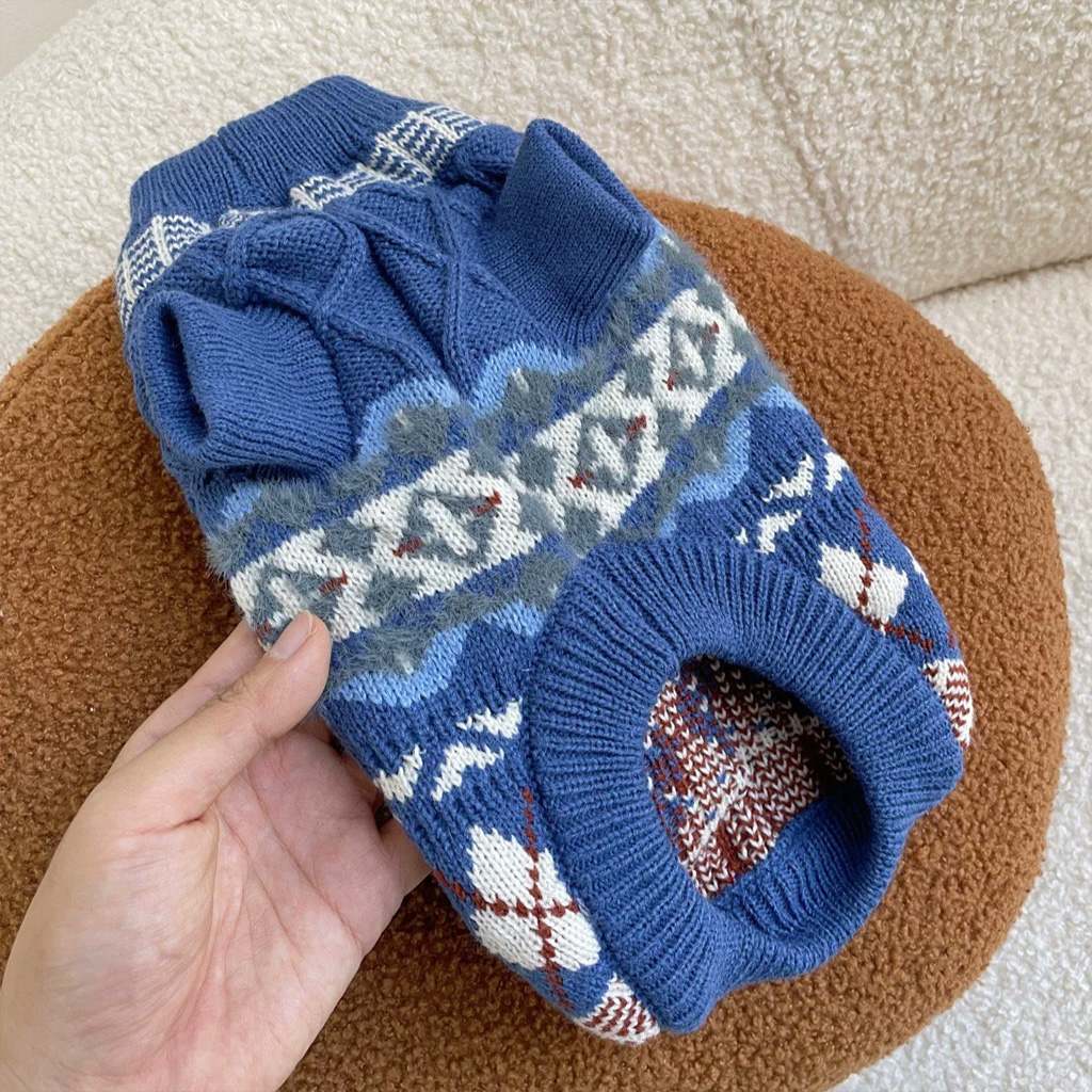 Denim blue Fair Isle knit pet sweater held over a cushion, showing ribbed belly opening and sleeve cuffs.