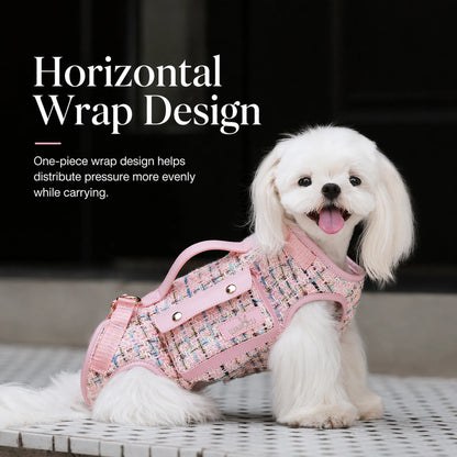 Small white dog wearing pink tweed dog carrier harness showing the horizontal one-piece wrap design with top handle