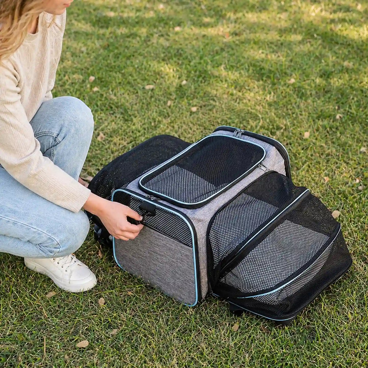 Owner kneeling beside fully expanded gray-and-blue pet carrier on grass