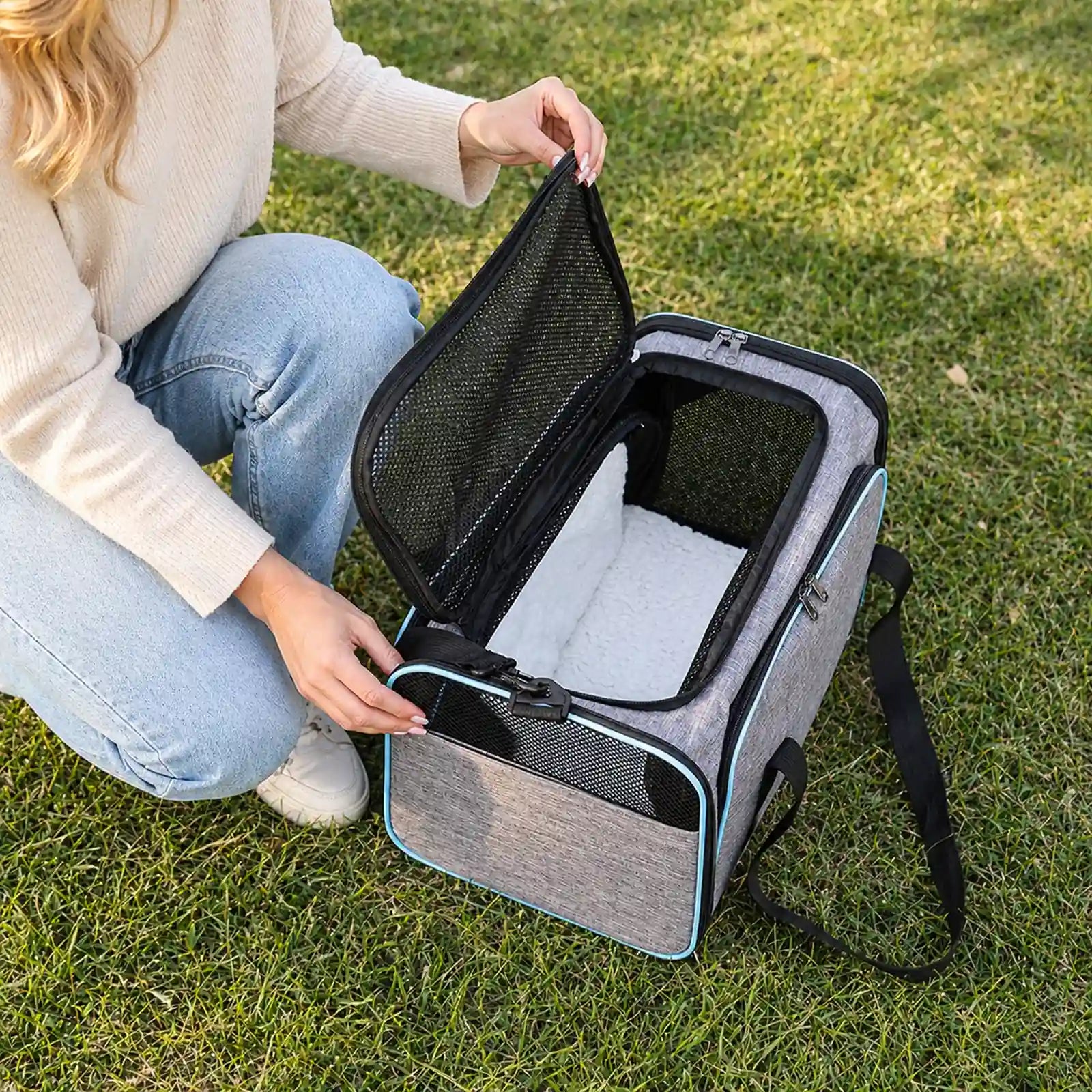 Owner lifting top mesh flap of gray-and-blue pet carrier to show plush mat